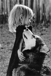 Black-and-white photo of me as a three- or four-year-old child. Oh, and I was blonde back then.'m standing next to a dog, Lightning, who is looking up at me. She's a Malamute who's almost as tall as I am. Oh, and I'm wearing a cape, like the little bad ass I was when I was that young.